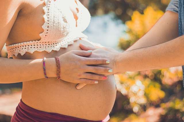 tripa al aire libre de una embarazada que tocan otras manos en verano