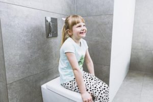 imagen de una niña sonriente sentada sobre un Wc cerrado para hablar de no tirar toallitas húmedas al WC