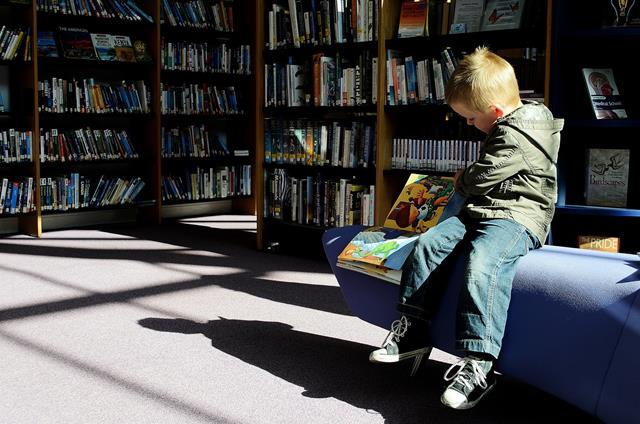 niño en biblioteca con libros y con zapatillas deportivas